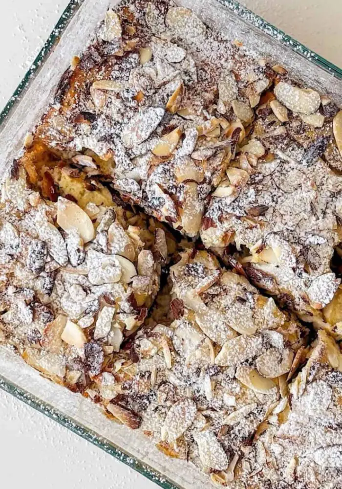 A bowl of baked almond oats topped with flaked almonds and a drizzle of honey, served warm with a spoon. The golden-brown oat bake has a soft, fluffy texture and is garnished with fresh berries for a wholesome breakfast.